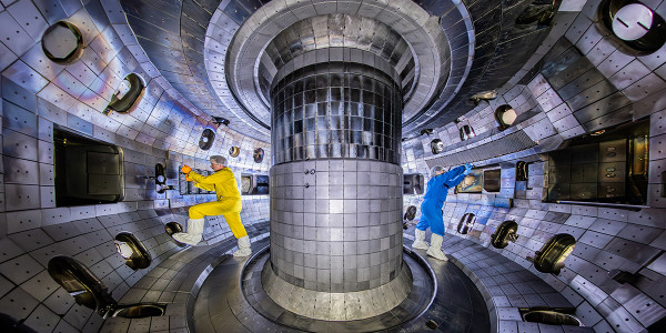 Two people in colored jumpsuits inside a curving conical metal scientific instrument
