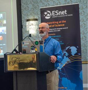 Person stands speaking at podium, with ESnet banner and presentation screen behind them.