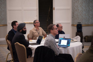 People in a conference room sitting around a large table, all looking to the front of the room