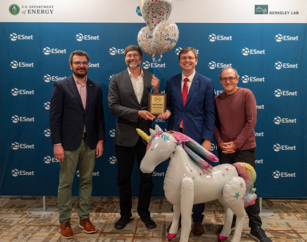 4 men posing with a plaque and a unicorn balloon