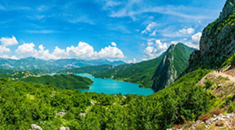 Bright blue lake and skies, surrounded by forested mountains