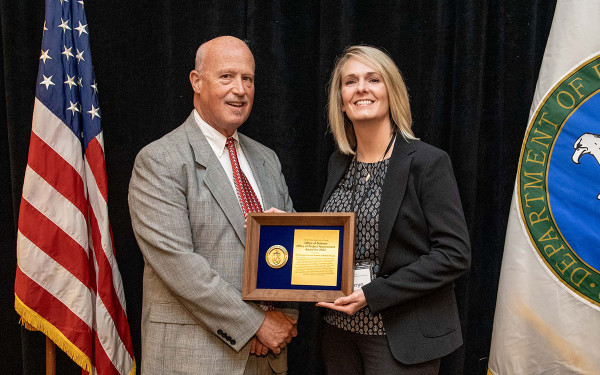 Man presenting award to woman flanked by flags